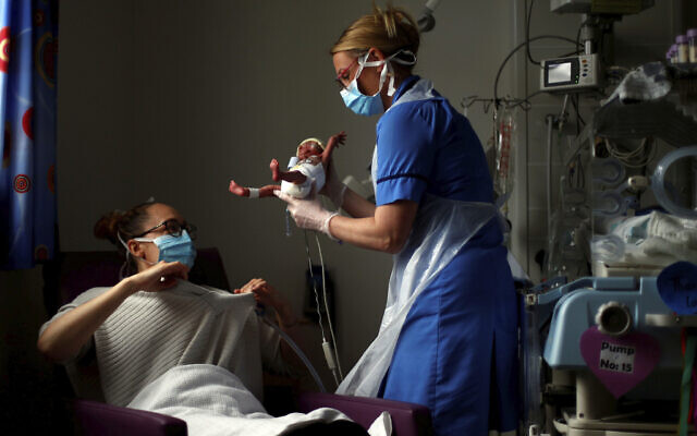 Illustration : une infirmière en néonatalogie remet un bébé à sa mère pendant la pandémie de coronavirus. (Crédit : Hannah McKay/Pool Photo via AP)
