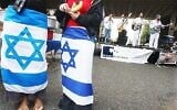 Illustration : Deux jeunes femmes arborant des drapeaux d'Israël autour de la taille tandis qu'un groupe de musique juif se produit lors d'un rassemblement pro-Israël sur le campus de l'université Rutgers à New Brunswick, dans le New Jersey, le 10 octobre 2003. (Crédit : Daniel Hulshizer/AP)