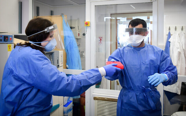 Le personnel médical de l'hôpital Barzilai, dans la ville d'Ashkelon, dans le sud d'Israël, portait des équipements de protection alors qu'il manipulait un échantillon de test de coronavirus le 29 mars 2020. (Crédit : Flash90) Le personnel médical de l'hôpital Barzilai, dans la ville d'Ashkelon, dans le sud d'Israël, portait des équipements de protection alors qu'il manipulait un échantillon de test de coronavirus le 29 mars 2020. (Crédit : Flash90)