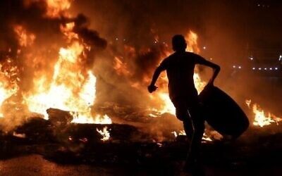 Un jeune Palestinien porte un pneu avant de l'incendier, lors d'affrontements avec les forces de sécurité israéliennes à la suite d'un rassemblement de soutien aux prisonniers palestiniens détenus dans les prisons israéliennes, au poste de contrôle de Hawara près de la ville cisjordanienne de Naplouse, le 8 septembre 2021. (Photo par Jaafar ASHTIYEH / AFP)
