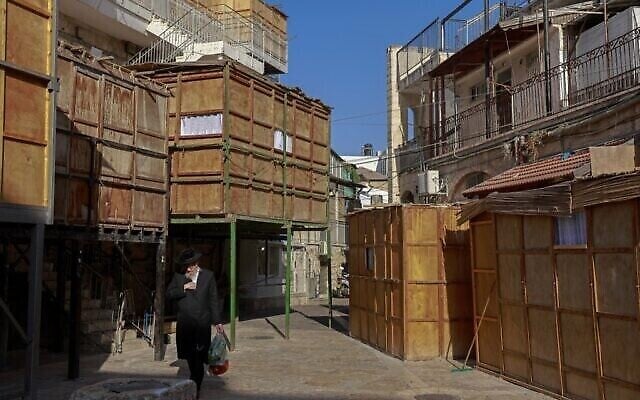 Un ultra-orthodoxe marche devant une souccah, une hutte temporaire construite à l'occasion de la fête juive de Souccot, fête des Tabernacles,  dans le quartier ultra-orthodoxe de Batei Ungarin près du quartier Mea Sharim à Jérusalem, le 20 septembre 2021. (Crédit :  MENAHEM KAHANA / AFP)