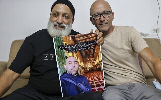 Malek Hassuna (à gauche) montre une photo de son défunt fils Mussa (au centre), abattu le 10 mai, alors qu'il est avec Effi Yehoshua à Lod, le 18 août 2021. (Crédit : AHMAD GHARABLI / AFP)