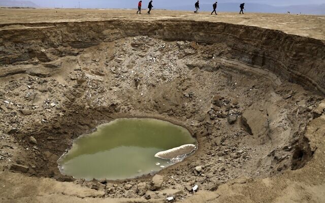 Des randonneurs marchent à côté de dolines dans une zone de mer asséchée qui a exposé et créé une plaine salée, à environ 20 km au sud du kibboutz israélien Ein Gedi, dans la partie sud de la mer Morte, le 15 janvier 2021. (Crédit : Menahem KAHANA / AFP)