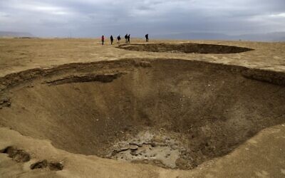Des randonneurs marchent à côté de dolines dans une zone de mer asséchée qui a exposé et créé une plaine salée, à environ 20 km au sud du kibboutz israélien Ein Gedi, dans la partie sud de la mer Morte, le 15 janvier 2021. (Crédit : Menahem KAHANA / AFP)