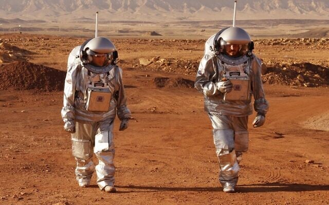 Un couple d'astronautes d'une équipe d'Europe et d'Israël marche en combinaison spatiale lors d'une mission d'entraînement pour la planète Mars sur un site qui simule une station hors site au cratère Ramon à Mitzpe Ramon, dans le sud du désert du Néguev en Israël, le 10 octobre 2021. (Crédit : JACK GUEZ / AFP)