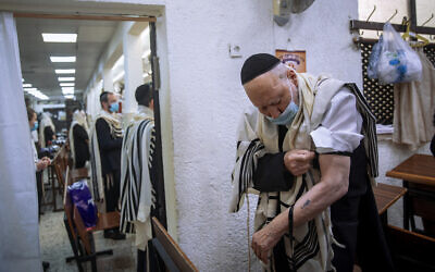 Le survivant de la Shoah Yehoshua Datsinger place ses tefillin sur son bras, au-dessus de son numéro d'identification tatoué à  Auschwitz , à Bnei Brak, le 21 septembre 2020. (Crédit : AP Photo/Oded Balilty)