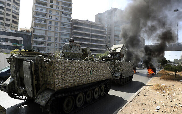 Des soldats de l'armée libanaise montent la garde sur leur véhicule blindé alors que des partisans des groupes chiites Hezbollah et Amal brûlent des conteneurs à ordures pour bloquer une route lors d'une manifestation à Beyrouth, au Liban, jeudi 14 octobre 2021. (Crédit : AP Photo/Bilal Hussein) Des soldats de l'armée libanaise montent la garde sur leur véhicule blindé alors que des partisans des groupes chiites Hezbollah et Amal brûlent des conteneurs à ordures pour bloquer une route lors d'une manifestation à Beyrouth, au Liban, jeudi 14 octobre 2021. (Crédit : AP Photo/Bilal Hussein)