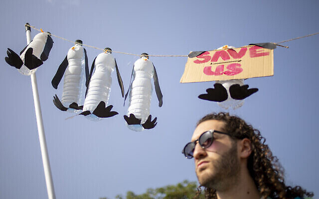 Un homme tient une affiche représentant des pingouins morts lors d'une marche demandant aux dirigeants mondiaux de prendre des mesures pour inverser le changement climatique et arrêter l'utilisation des combustibles fossiles à Tel Aviv, le 29 octobre 2021. (AP Photo/Ariel Schalit)