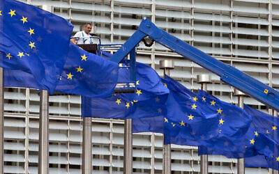 Sur cette photo d'archives du 23 juin 2016, un ouvrier sur un ascenseur ajuste les drapeaux de l'UE devant le siège de l'UE à Bruxelles. (Crédit : Virginia Mayo/AP)