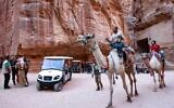 Des touristes montent sur des chameaux et d'autres sur une charrette électrique, lors de leur voyage dans la célèbre cité antique de Petra en Jordanie, à quelque 230 km au sud de la capitale Amman, le 27 octobre 2021. (Crédit : Khalil MAZRAAWI / AFP)