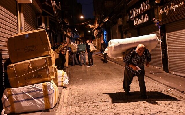 Un porteur porte des affaires dans une rue tandis que d'autres attendent leur tour tôt le matin, le 28 octobre 2021, près du Grand Bazar d'Istanbul. (Crédit : Ozan KOSE / AFP)