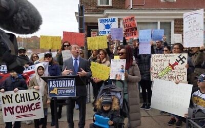 Un manifestant, à droite, brandit une pancarte avec une croix gammée lors d'une manifestation anti-vaccins devant le bureau du député du Bronx Jeffrey Dinowitz, le 14 novembre 2021. L'ancien exécutif du comté de Westchester et candidat au poste de gouverneur, Rob Astorino, au podium, a pris la parole lors du rassemblement. (Crédit : autorisation de Jeffrey Dinowitz, via Twitter)
