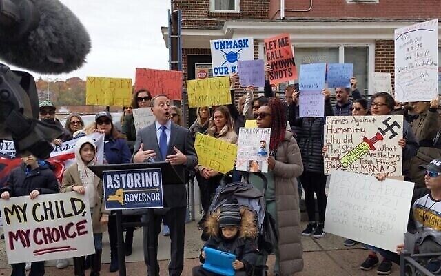 Un manifestant, à droite, brandit une pancarte avec une croix gammée lors d'une manifestation anti-vaccins devant le bureau du député du Bronx Jeffrey Dinowitz, le 14 novembre 2021. L'ancien exécutif du comté de Westchester et candidat au poste de gouverneur, Rob Astorino, au podium, a pris la parole lors du rassemblement. (Crédit : autorisation de Jeffrey Dinowitz, via Twitter) Un manifestant, à droite, brandit une pancarte avec une croix gammée lors d'une manifestation anti-vaccins devant le bureau du député du Bronx Jeffrey Dinowitz, le 14 novembre 2021. L'ancien exécutif du comté de Westchester et candidat au poste de gouverneur, Rob Astorino, au podium, a pris la parole lors du rassemblement. (Crédit : autorisation de Jeffrey Dinowitz, via Twitter)