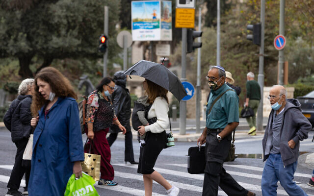 Des Israéliens portant des masques se protègent de la pluie sur Jaffa Road, à Jérusalem, le 31 octobre 2021. (Crédit : Olivier Fitoussi/Flash90) Des Israéliens portant des masques se protègent de la pluie sur Jaffa Road, à Jérusalem, le 31 octobre 2021. (Crédit : Olivier Fitoussi/Flash90)