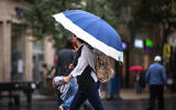 Des Israéliens se protègent de la pluie sur Jaffa Road, dans le centre de Jérusalem, le 31 octobre 2021. (Crédit : Olivier Fitoussi/Flash90)