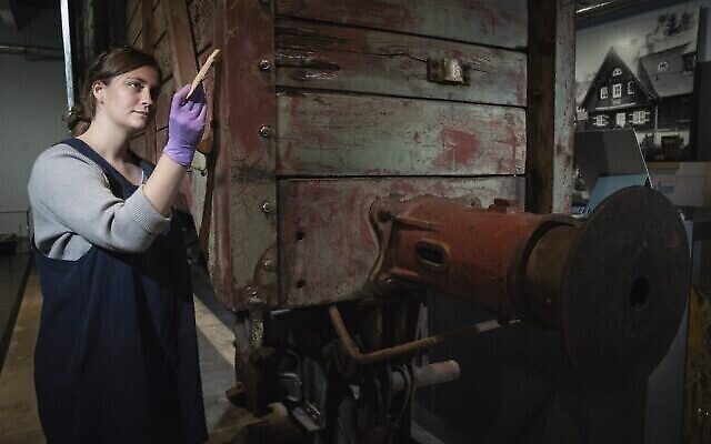Emily Thomas, technicienne en conservation, nettoie un wagon du type utilisé pour transporter les victimes vers les camps de la mort dans la galerie de la Shoah de l'Imperial War Museum à Londres, le 30 septembre 2021. (Crédit : avec l'aimable autorisation de l'Imperial War Museum)