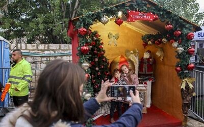 Des enfants posent pour des photos près d'une crèche avec un arbre de Noël et Saint Nicolas dans le centre-ville de Nazareth, dans le nord d'Israël, le 18 décembre 2021. (Crédit : AHMAD GHARABLI / AFP)