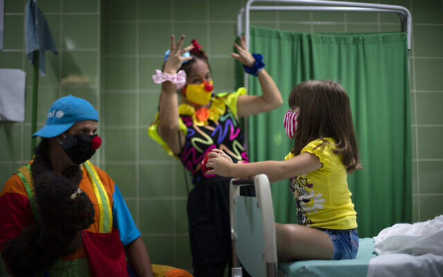 Des clowns divertissent une fillette qui attend dans la salle de contrôle après s'être fait injecter une dose du vaccin Soberana-02 contre le COVID-19 à La Havane, Cuba, le 24 août 2021. (Crédit :AP Photo/Ramon Espinosa) Des clowns divertissent une fillette qui attend dans la salle de contrôle après s'être fait injecter une dose du vaccin Soberana-02 contre le COVID-19 à La Havane, Cuba, le 24 août 2021. (Crédit :AP Photo/Ramon Espinosa)