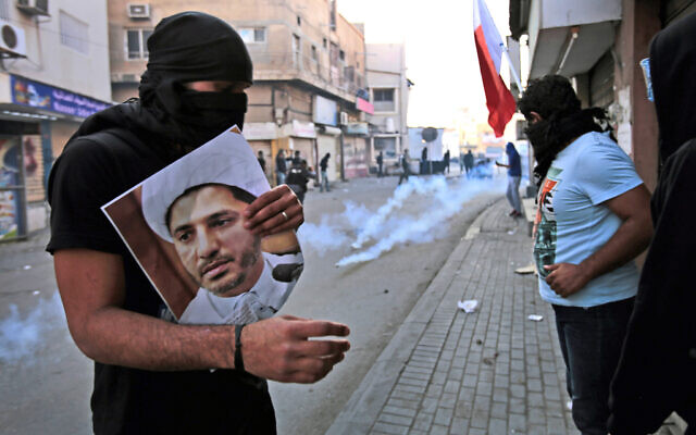 Un manifestant anti-gouvernemental bahreïni masqué tient une photo du chef religieux chiite emprisonné Cheikh Ali Salman, chef de l'association politique d'opposition al-Wefaq, alors que la police anti-émeute tire des grenades lacrymogènes lors d'affrontements à Bilad Al Qadeem, au Bahreïn, le 3 janvier 2015. (Crédit : AP Photo/Hasan Jamali, Dossier) Un manifestant anti-gouvernemental bahreïni masqué tient une photo du chef religieux chiite emprisonné Cheikh Ali Salman, chef de l'association politique d'opposition al-Wefaq, alors que la police anti-émeute tire des grenades lacrymogènes lors d'affrontements à Bilad Al Qadeem, au Bahreïn, le 3 janvier 2015. (Crédit : AP Photo/Hasan Jamali, Dossier)