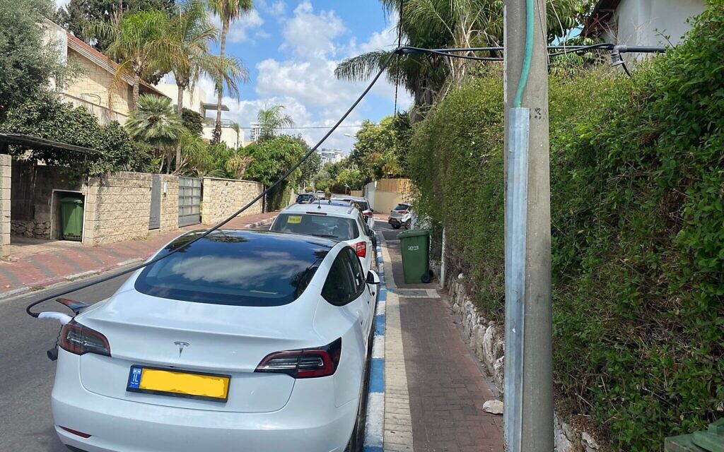 Une voiture Tesla est rechargée par le biais d'un système artisanal de câbles provenant de l'intérieur d'une habitation de Ramat Gan jusqu'à une place publique de stationnement, le 8 décembre 2021. (Autorisation : Sharon B.) Une voiture Tesla est rechargée par le biais d'un système artisanal de câbles provenant de l'intérieur d'une habitation de Ramat Gan jusqu'à une place publique de stationnement, le 8 décembre 2021. (Autorisation : Sharon B.)