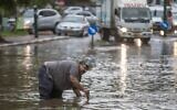 Un Israélien tente d'ouvrir une bouche d'égout alors que l'eau inonde une rue pendant un orage à Netanya, au nord de Tel Aviv, le 25 octobre 2015. (Crédit : AFP/Jack Guez)