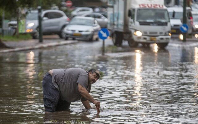 Un Israélien tente d'ouvrir une bouche d'égout alors que l'eau inonde une rue pendant un orage à Netanya, au nord de Tel Aviv, le 25 octobre 2015. (Crédit : AFP/Jack Guez) Un Israélien tente d'ouvrir une bouche d'égout alors que l'eau inonde une rue pendant un orage à Netanya, au nord de Tel Aviv, le 25 octobre 2015. (Crédit : AFP/Jack Guez)