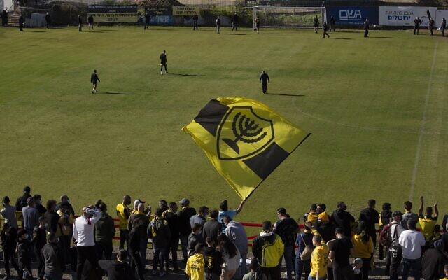 Les supporters du Beitar FC chantent et brandissent leur drapeau après l'entrée des joueurs sur le terrain lors d'un entraînement à Jérusalem, le 11 décembre 2020. (Crédit : AP Photo/Maya Alleruzzo) Les supporters du Beitar FC chantent et brandissent leur drapeau après l'entrée des joueurs sur le terrain lors d'un entraînement à Jérusalem, le 11 décembre 2020. (Crédit : AP Photo/Maya Alleruzzo)