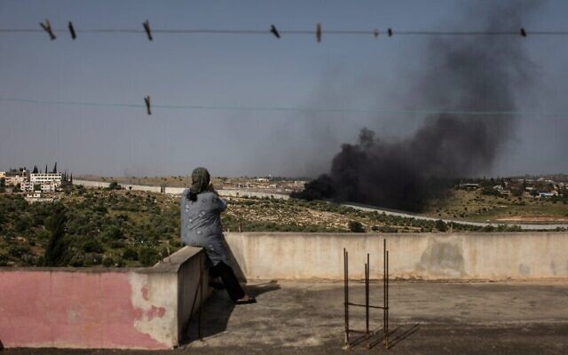 Maysoon Sweity, résidente de Beit Awwa de 54 ans, regardant les fumées noires d'un feu de déchets électroniques et d'ordure près du mur en béton qui sépare son village et Israël, le 26 avril 2019. (Crédit :  Tamir Kalifa)