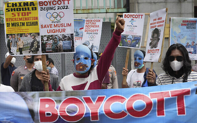 Des étudiants militants, dont certains portent des masques aux couleurs du drapeau indépendantiste du Turkestan oriental, crient des slogans lors d'un rassemblement pour protester contre les Jeux olympiques d'hiver de Pékin 2022, devant l'ambassade de Chine à Jakarta, en Indonésie, le 14 janvier 2022. (Crédit : AP Photo/Tatan Syuflana) Des étudiants militants, dont certains portent des masques aux couleurs du drapeau indépendantiste du Turkestan oriental, crient des slogans lors d'un rassemblement pour protester contre les Jeux olympiques d'hiver de Pékin 2022, devant l'ambassade de Chine à Jakarta, en Indonésie, le 14 janvier 2022. (Crédit : AP Photo/Tatan Syuflana)