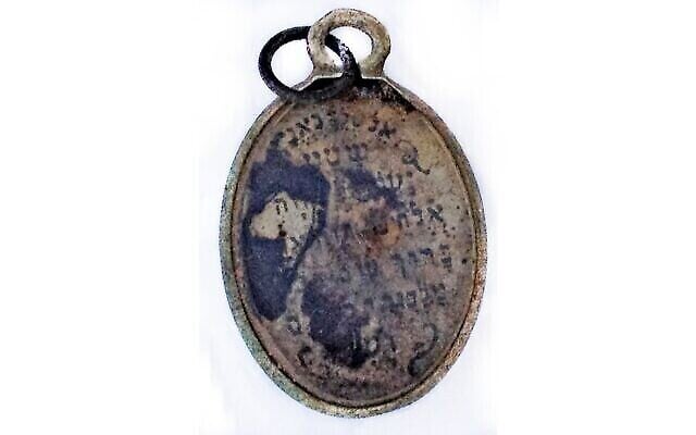 Un pendentif découvert dans le bâtiment où les victimes se déshabillaient avant d'être emmenées dans les chambres à gaz de Sobibor, sur lequel on peut lire : "Au roi fidèle, O Israël, notre Dieu est Un. Que soit béni le nom du roi glorieux pour les siècles des siècles. (Crédit : Yoram Haimi/IAA) Un pendentif découvert dans le bâtiment où les victimes se déshabillaient avant d'être emmenées dans les chambres à gaz de Sobibor, sur lequel on peut lire : "Au roi fidèle, O Israël, notre Dieu est Un. Que soit béni le nom du roi glorieux pour les siècles des siècles. (Crédit : Yoram Haimi/IAA)