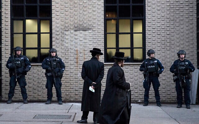 Dans cette photo d'archive du 11 décembre 2019, un groupe d'Orthodoxes passe devant des agents de la Police de New York en faction devant une synagogue de Brooklyn, peu de temps avant les obsèques de Mosche Deutsch, étudiant de Brooklyn abattu lors d'une fusillade sur un marché de Jersey City. (AP Photo/Mark Lennihan)