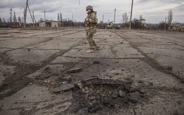 Un soldat ukrainien regarde un trou formé par un obus tiré par les séparatistes pro-russes dans le village de Novoluhanske, dans la région de Luhansk, en Ukraine, le 19 février 2022. (Crédit : AP Photo/Oleksandr Ratushniak) Un soldat ukrainien regarde un trou formé par un obus tiré par les séparatistes pro-russes dans le village de Novoluhanske, dans la région de Luhansk, en Ukraine, le 19 février 2022. (Crédit : AP Photo/Oleksandr Ratushniak)