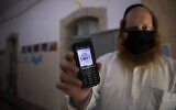 Un enseignant tenant son téléphone portable certifiant qu'il s'agit d'un téléphone "casher", à l'entrée d'une école ultra-orthodoxe, à Jérusalem, le 6 mai 2020. (Crédit : Nati Shohat/Flash90)