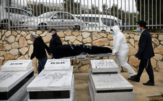 Un employé des services funéraires porte le corps de la survivante de la Shoah d'origine roumaine Golda Schwartz, décédée à l'âge de 93 ans des complications de la COVID-19, au cimetière Nof Hagalil, le 28 janvier 2021. (Crédit : Gili Yaari / Flash90) Un employé des services funéraires porte le corps de la survivante de la Shoah d'origine roumaine Golda Schwartz, décédée à l'âge de 93 ans des complications de la COVID-19, au cimetière Nof Hagalil, le 28 janvier 2021. (Crédit : Gili Yaari / Flash90)