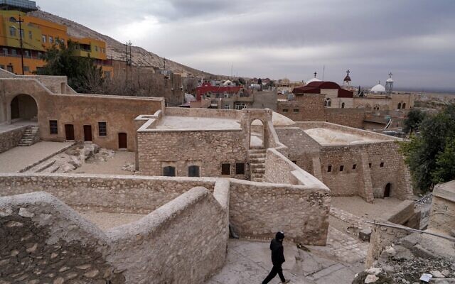 Un homme marche devant la synagogue Prophet Nahum (dont la forme actuelle date de 1796), avec l'église chaldéenne Mar Gorgis en arrière-plan, dans la ville d'al-Qosh, dans le nord de l'Irak, à environ 50 kilomètres au nord de Mossoul, le 3 février 2022. (Crédit : Ismael ADNAN / AFP)