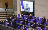 Des membres du gouvernement allemand, parmi lesquels le chancelier Olaf Scholz, en bas au centre, applaudissent lorsque le président ukrainien Volodymyr Zelensky apparaît sur un écran pour s'adresser par vidéoconférence à la chambre basse du parlement allemand, au Bundestag à Berlin, le 17 mars 2022. (Crédit : Tobias Schwarz/AFP)