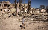 Un enfant marche devant une école endommagée dans la ville de Zhytomyr, dans le nord de l’Ukraine, le 23 mars 2022. (Crédit : Fadel Senna/AFP)