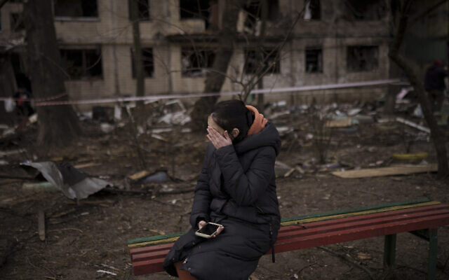 Une habitante assise à l'extérieur d'un bâtiment détruit après avoir été touché par des tirs d'artillerie à Kiev, en Ukraine, lundi 14 mars 2022. (Crédit : Felipe Dana/AP Photo)