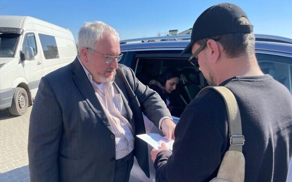 Le consul israélien Alon Shoham (à gauche) délivre un laissez-passer — établi dans la voiture derrière eux — à un citoyen israélo-ukrainien, près de Krakovets, au poste frontalier entre l’Ukraine et la Pologne, le 23 mars 2022. (Crédit : Carrie Keller-Lynn/The Times of Israel)