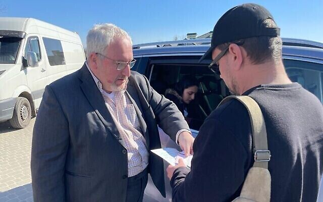 Le consul israélien Alon Shoham (à gauche) délivre un laissez-passer — établi dans la voiture derrière eux — à un citoyen israélo-ukrainien, près de Krakovets, au poste frontalier entre l’Ukraine et la Pologne, le 23 mars 2022. (Crédit : Carrie Keller-Lynn/The Times of Israel)