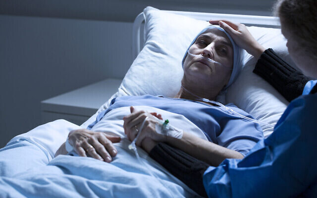 Un bénévole au chevet d'une femme mourant d'une tumeur dans une chambre d'hôpital. (Crédit : iStock) Un bénévole au chevet d'une femme mourant d'une tumeur dans une chambre d'hôpital. (Crédit : iStock)
