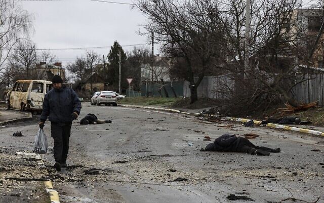 Un homme marche dans une rue au mileiu de plusieurs cadavres au sol à Bucha, au nord-ouest de Kiev, en Ukraine, le 2 avril 2022. (Crédit : RONALDO SCHEMIDT / AFP)