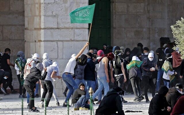 Des Palestiniens, dont l'un brandit un drapeau du Hamas, affrontent la police israélienne au mont du Temple à Jérusalem, le 22 avril 2022. (Crédit : Ahmad Gharabli/AFP)