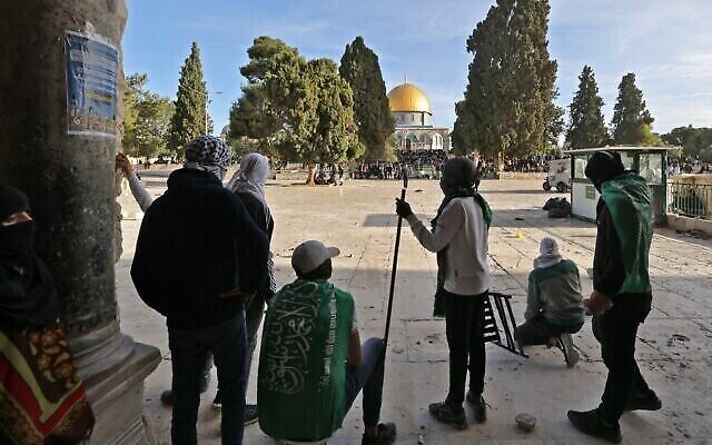 Des Palestiniens enveloppés de drapeaux du Hamas prennent position dans la cour de l’enceinte du mont du Temple, dans la Vieille Ville de Jérusalem, lors d’affrontements avec la police israélienne, le 22 avril 2022. (Crédit : Ahmad Gharabli/AFP)
