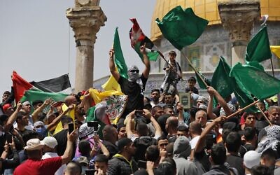 Des Palestiniens brandissent des drapeaux palestiniens et islamiques lors d'un rassemblement à la mosquée Al-Aqsa sur le Mont du Temple à Jérusalem, après la dernière prière du vendredi du mois sacré musulman du Ramadan, le 29 avril 2022. (Crédit : Ahmad GHARABLI / AFP)