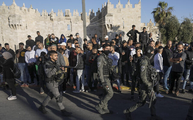 Des Palestiniens regardent les forces de sécurité israéliennes patrouiller près de la porte de Damas, juste à l'extérieur de la vieille ville de Jérusalem, le 20 avril 2022. (Crédit: AP/Mahmoud Illean) Des Palestiniens regardent les forces de sécurité israéliennes patrouiller près de la porte de Damas, juste à l'extérieur de la vieille ville de Jérusalem, le 20 avril 2022. (Crédit: AP/Mahmoud Illean)