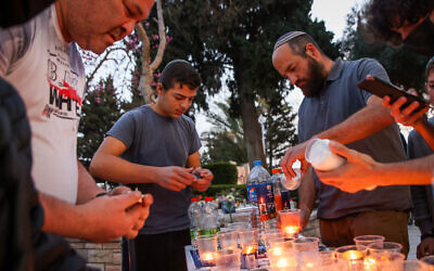 Des hommes juifs allument des bougies après les funérailles du policier Amir Khoury lors de ses funérailles à Nof Hagalil, le 31 mars 2022. (Crédit : David Cohen/Flash90)