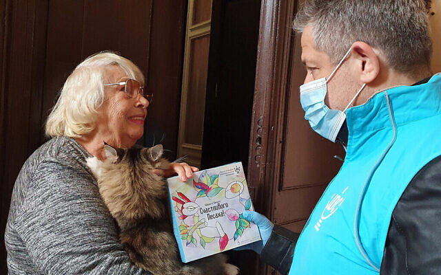 Svetlana Niselevitch reçoit une haggadah pour Pessah d’un membre du personnel de JDC devant son domicile à Odessa, en Ukraine, le 8 avril 2022. (Crédit : JDC par l'intermédiaire de la JTA)