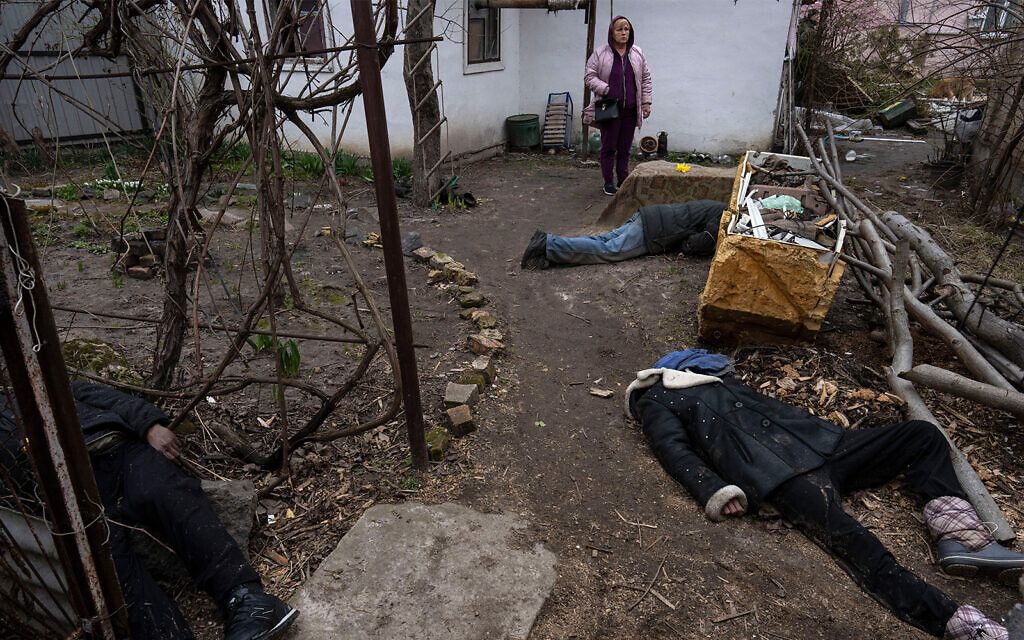 Une femme se tient à côté de trois corps dans la cour d'une maison à Bucha, dans la banlieue de Kiev, en Ukraine, le 5 avril 2022. (Crédit : AP Photo/Rodrigo Abd) Une femme se tient à côté de trois corps dans la cour d'une maison à Bucha, dans la banlieue de Kiev, en Ukraine, le 5 avril 2022. (Crédit : AP Photo/Rodrigo Abd)
