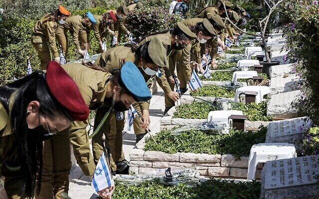 Le 13 avril 2021, au cimetière militaire de Kiryat Shaul, dans la ville côtière méditerranéenne de Tel-Aviv, des soldats placent des drapeaux israéliens arborant des ceintures noires au-dessus du mot hébreu « Souvenir » sur des tombes, en hommage aux soldats tombés le jour du Yom HaZikaron. (Crédit : Jack Guez/AFP) Le 13 avril 2021, au cimetière militaire de Kiryat Shaul, dans la ville côtière méditerranéenne de Tel-Aviv, des soldats placent des drapeaux israéliens arborant des ceintures noires au-dessus du mot hébreu « Souvenir » sur des tombes, en hommage aux soldats tombés le jour du Yom HaZikaron. (Crédit : Jack Guez/AFP)